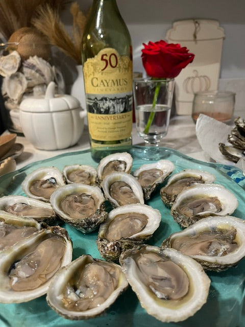 Platter of oysters with a bottle of Caymus wine and a red rose in the background.